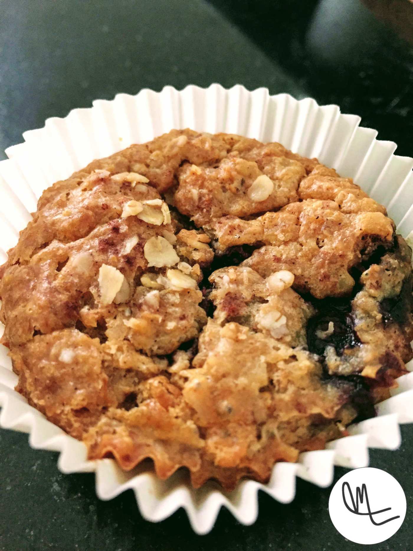 Oat blueberry muffin in a muffin paper cup, sprinkled with a few oats.